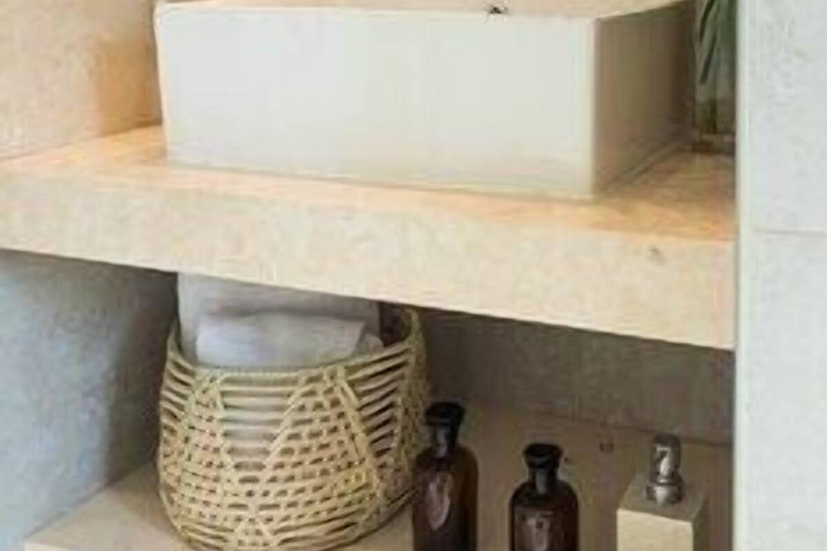 A bathroom with a white sink, a hairdryer, a mirror, a potted plant, and a shelf with bottles and a woven basket.
