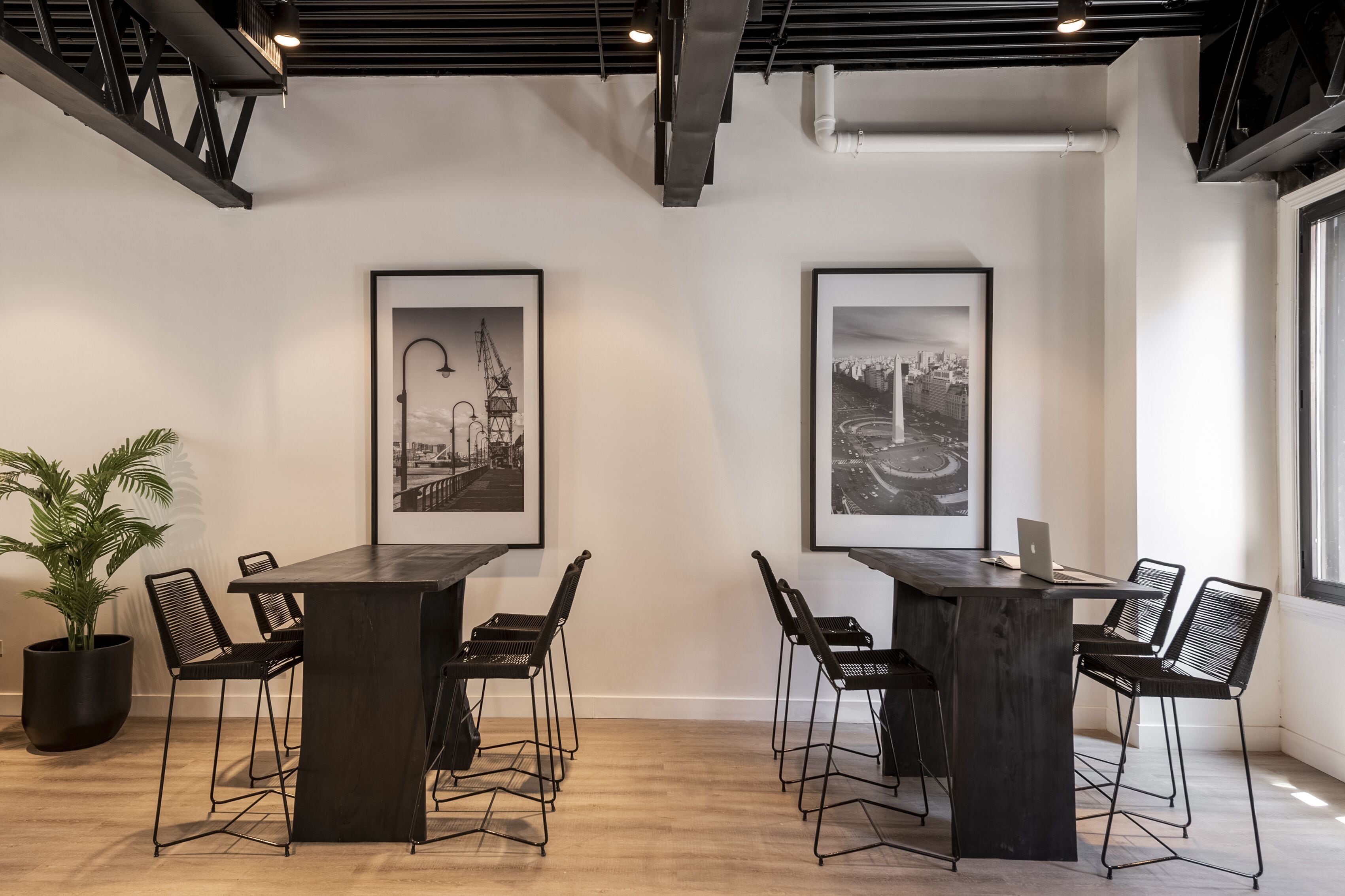 Un salón de conferencias moderno con una mesa de madera oscura y sillas metálicas, fotografías en blanco y negro enmarcadas en las paredes y una planta en maceta a la izquierda.