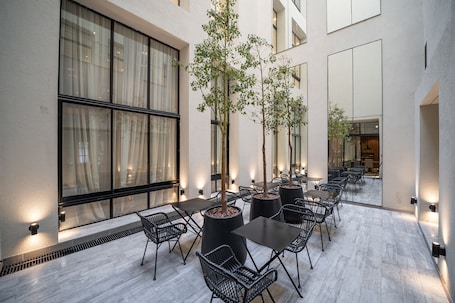 An outdoor patio with tables and chairs, large windows, and potted trees.
