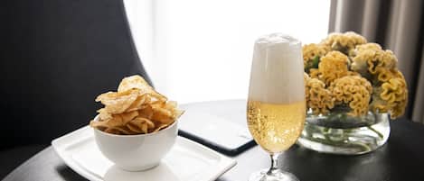A white bowl of chips on a white plate, a glass of champagne, and a vase of yellow flowers on a dark table.