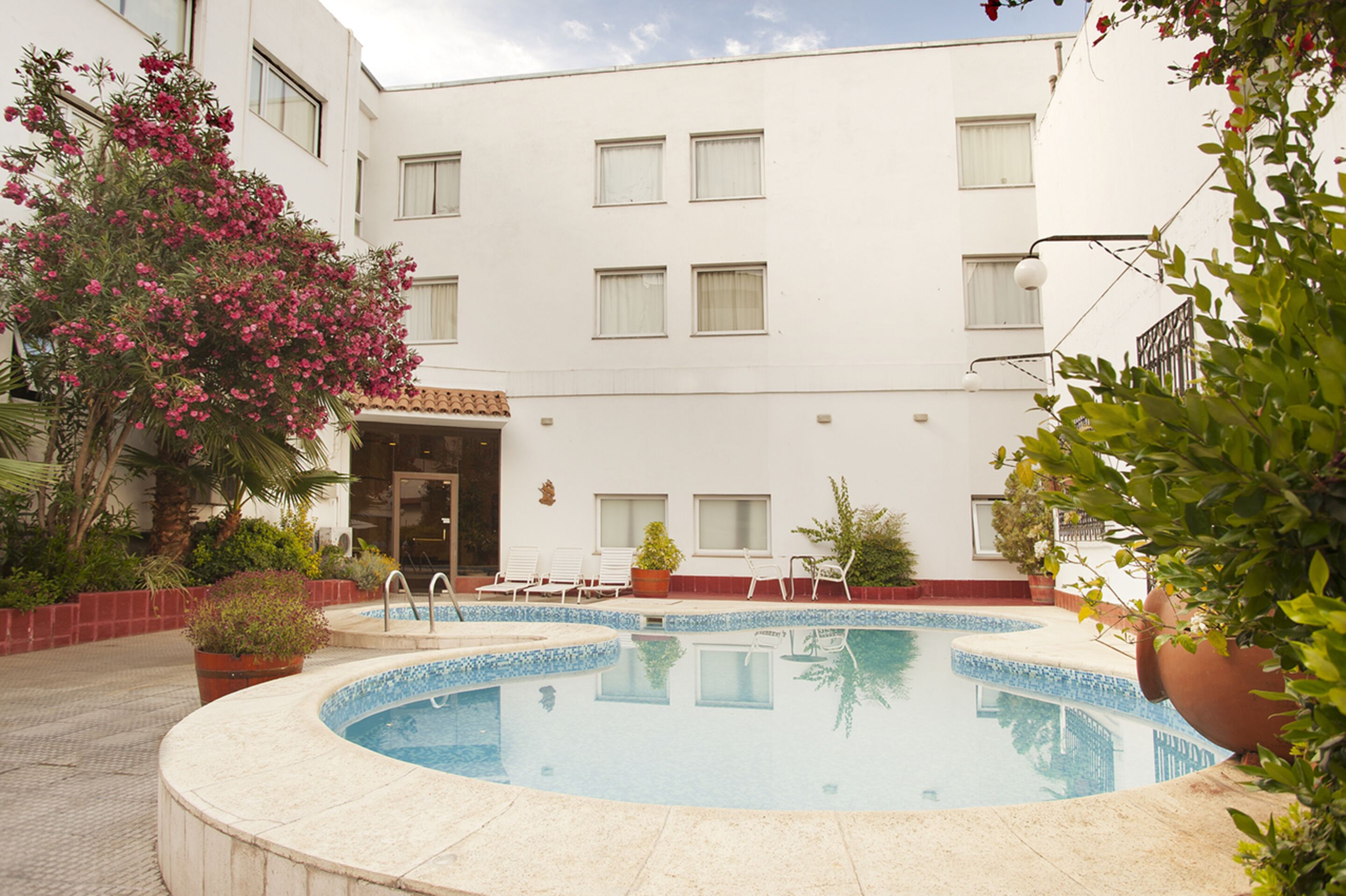 Un espace piscine doté d’une terrasse carrelée, de chaises longues et de plantes en pot.