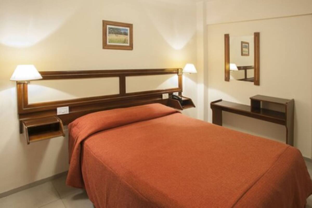 A hotel room with a single bed, bedside tables, lamps, and a mirror.