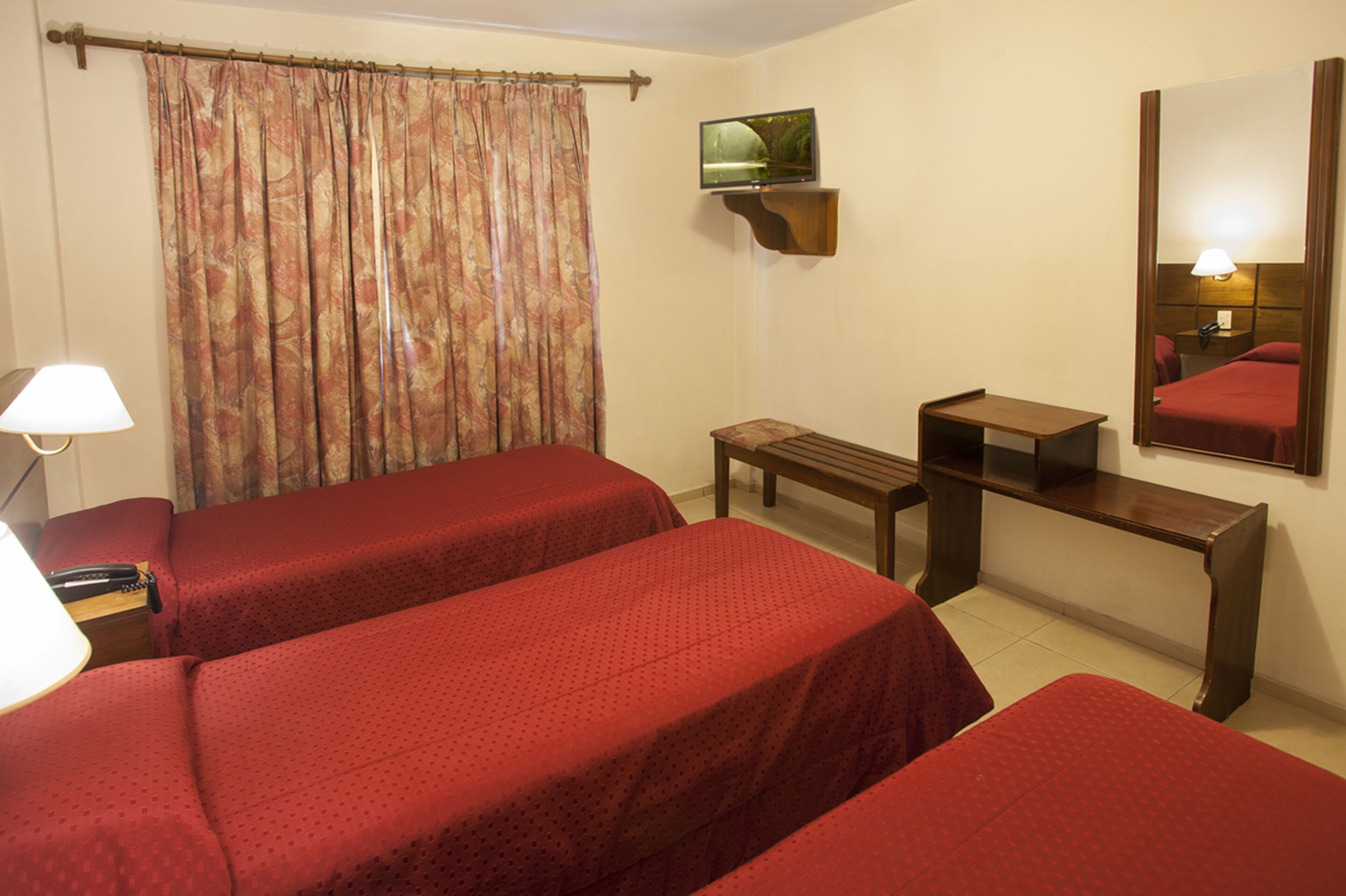 A hotel room with two single beds, a TV mounted on the wall, a desk, and a mirror.