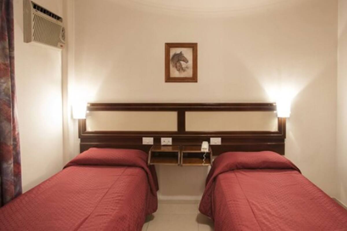 A hotel room with two single beds, a headboard with a mounted picture, bedside lamps, and a small table with a phone and a lamp.