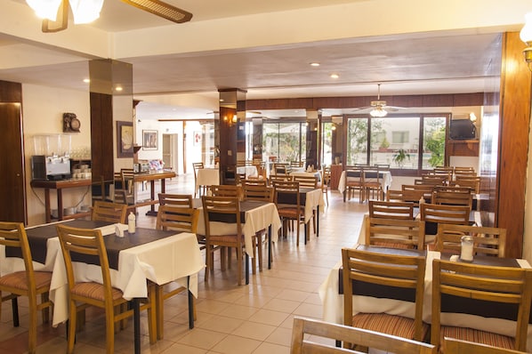 Un comedor amplio con varias mesas y sillas, una estación de café y ventanas grandes que aportan luz natural.
