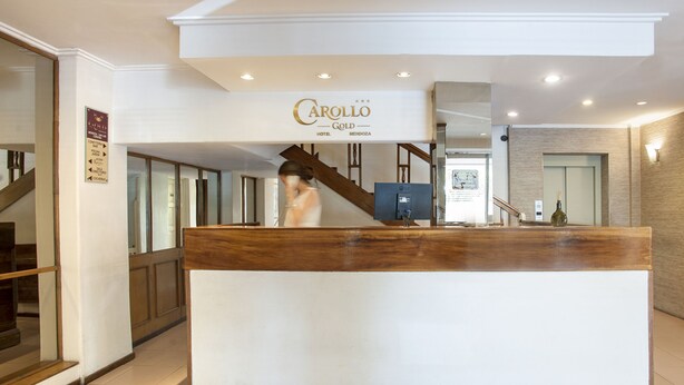 Un comptoir d’accueil en bois se trouve dans le hall du Carollo Gold Hotel à Mendoza, avec une enseigne placée au-dessus.
