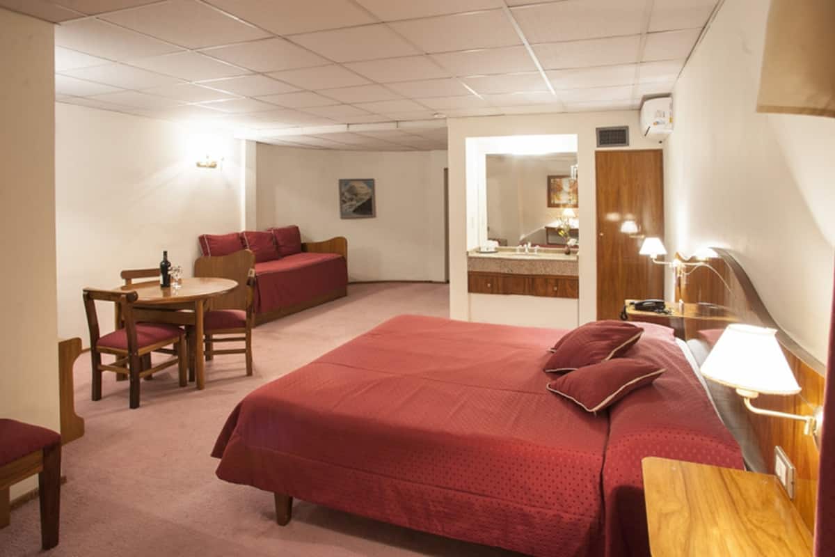 Une chambre d’hôtel avec un grand lit, un bureau avec une chaise, une petite table, un canapé, un miroir et une lampe.