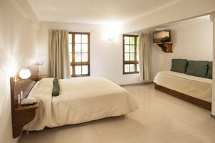 Habitación de hotel con cama, mesita de noche con lámpara, sofá y televisor montado en la pared.