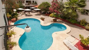 Ein Schwimmbecken mit ungewöhnlicher Form, umgeben von Topfpflanzen und Gartenmöbeln.