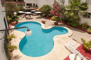 Una piscina de forma original, rodeada de plantas en macetas y mobiliario exterior.