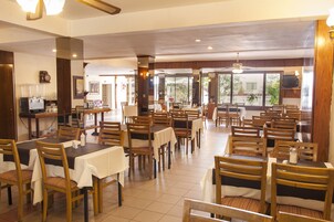 Un comedor amplio con varias mesas y sillas, una estación de café y ventanas grandes que aportan luz natural.