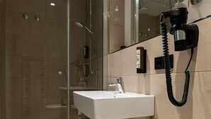 A modern bathroom with a glass shower enclosure, a white sink, and a mounted hairdryer. - ParkHotel Fulda (Fulda)