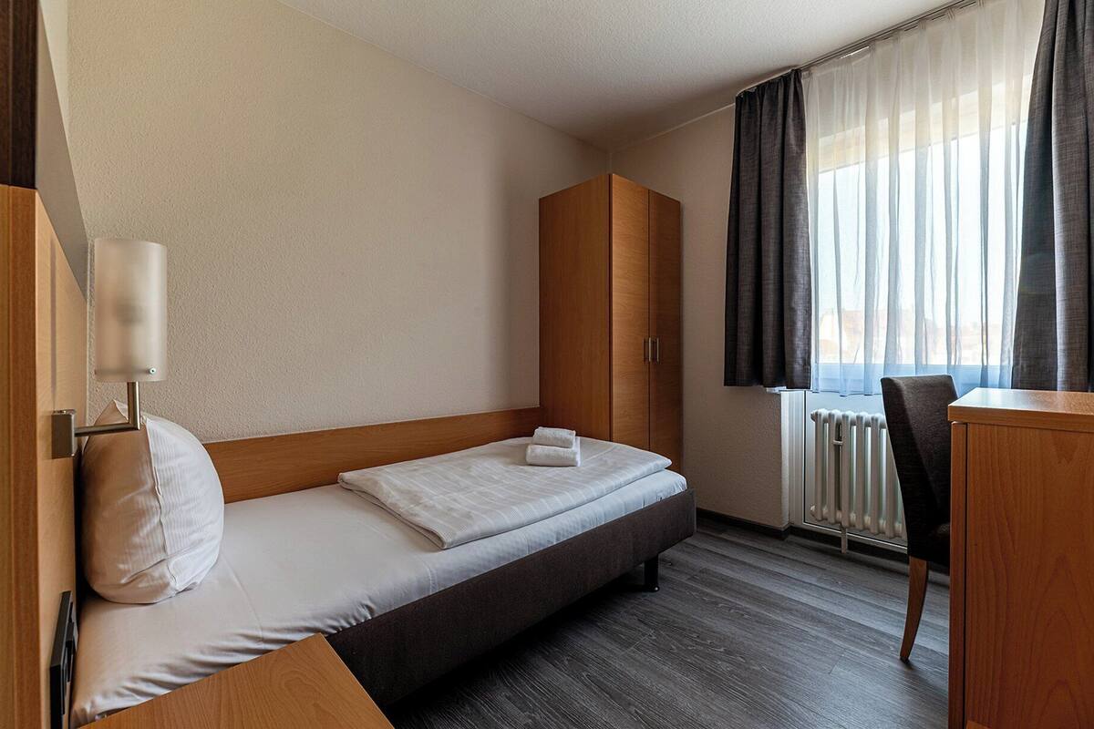 Une chambre d’hôtel avec un lit, une armoire en bois, un bureau et une chaise.