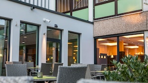 An outdoor seating area with wicker chairs and tables, large windows, and a building with a modern design.