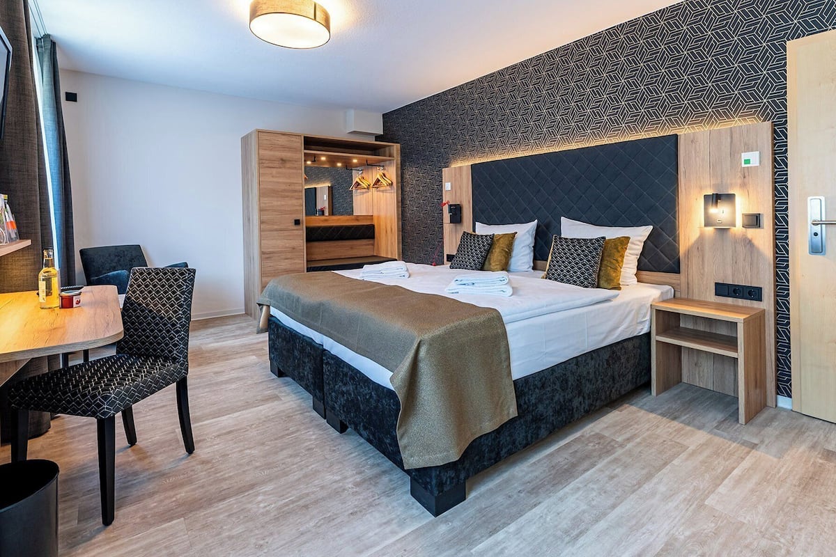 Une chambre d’hôtel moderne, dotée d’un grand lit, d’un bureau avec une chaise, d’une armoire et d’une petite table de chevet.