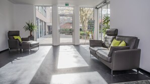 A modern lobby with a reception desk, two leather sofas, a potted plant, and a glass door leading outside.