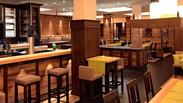 A modern restaurant with a bar area, wooden decor, and multiple seating options.
