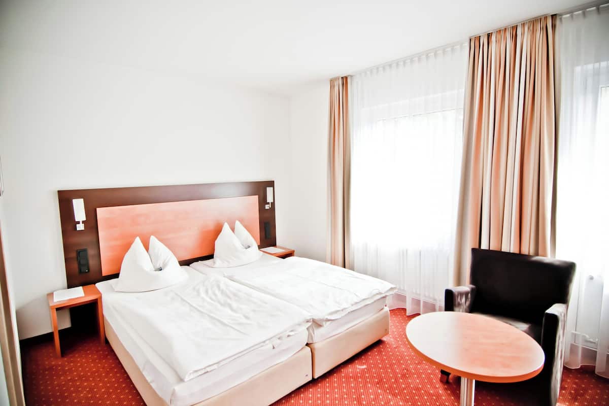 Une chambre d’hôtel avec un lit double, une petite table, une chaise et une grande fenêtre avec des rideaux.