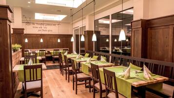 A restaurant interior with wooden furniture, green tablecloths, and pendant lighting.