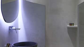 Un baño moderno con un espejo grande, un lavabo redondo, una ducha y un estante pequeño con artículos de aseo.