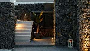 Interior de paredes de piedra con una escalera que conduce a una habitación oscura, una planta en maceta y un farol.