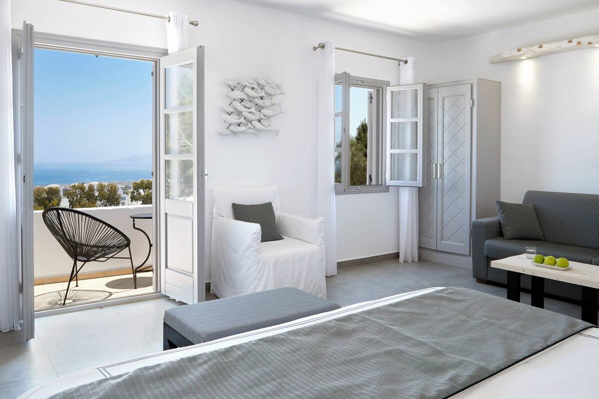 Un dormitorio moderno con balcón, cama, sofá y mesa de comedor.