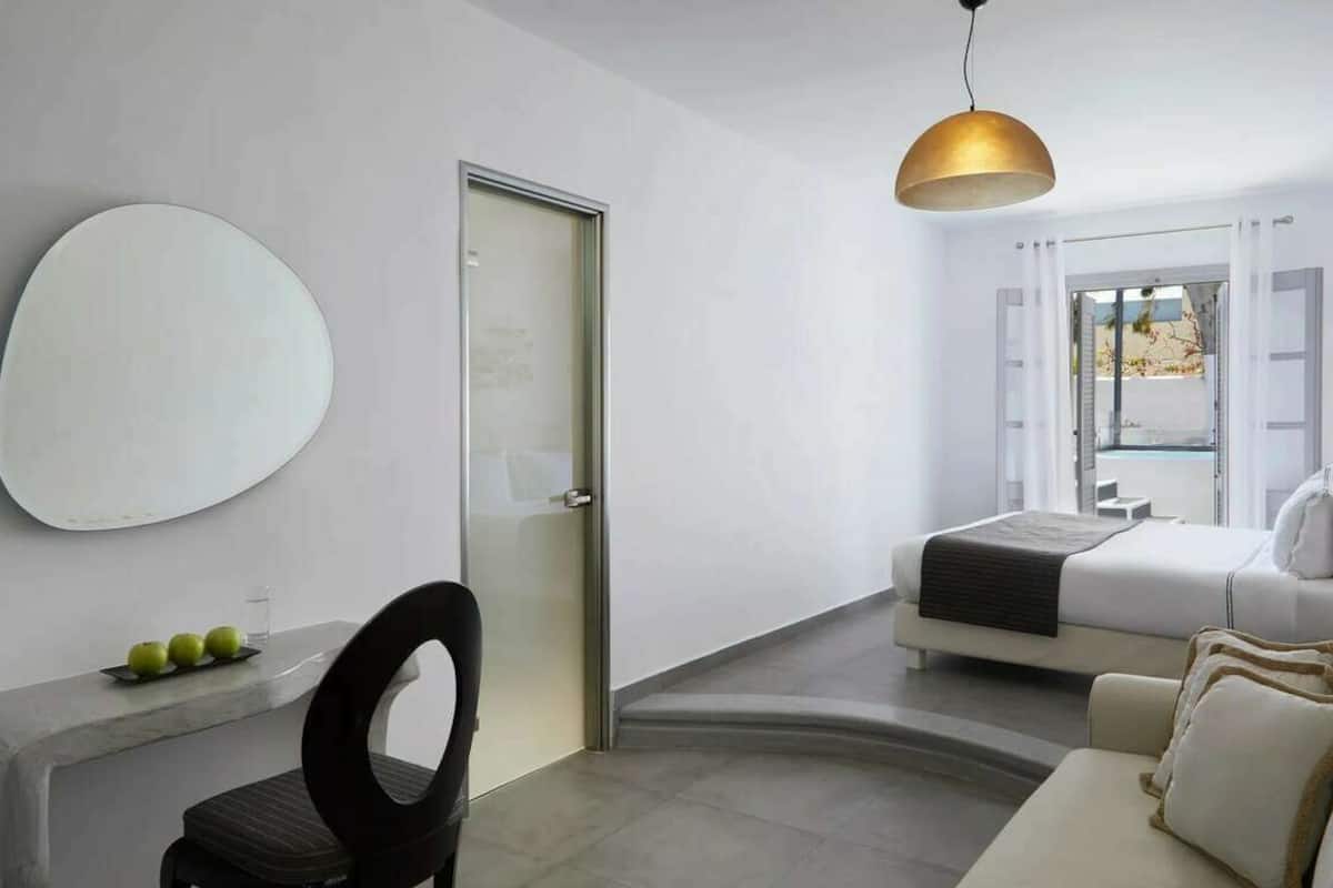 Habitación de hotel moderna con cama, escritorio y silla, espejo redondo y vistas al exterior.