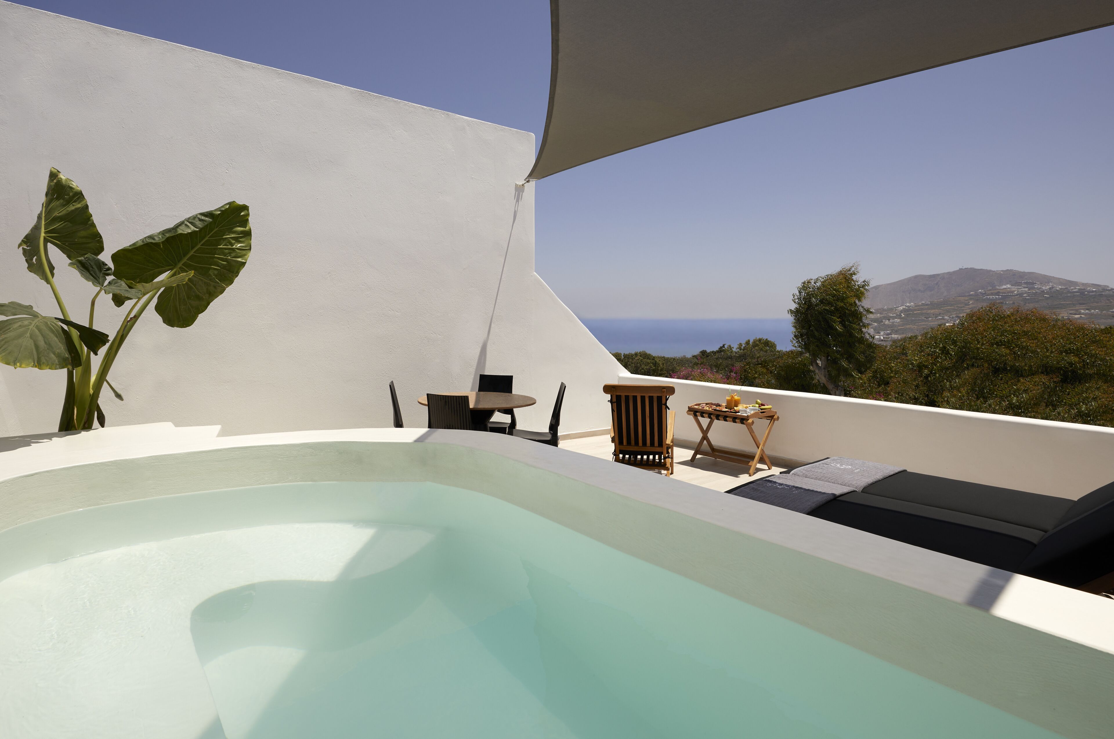 Piscina infinita no terraço, com vista para o mar e montanhas, rodeada por mobili ário de exterior.