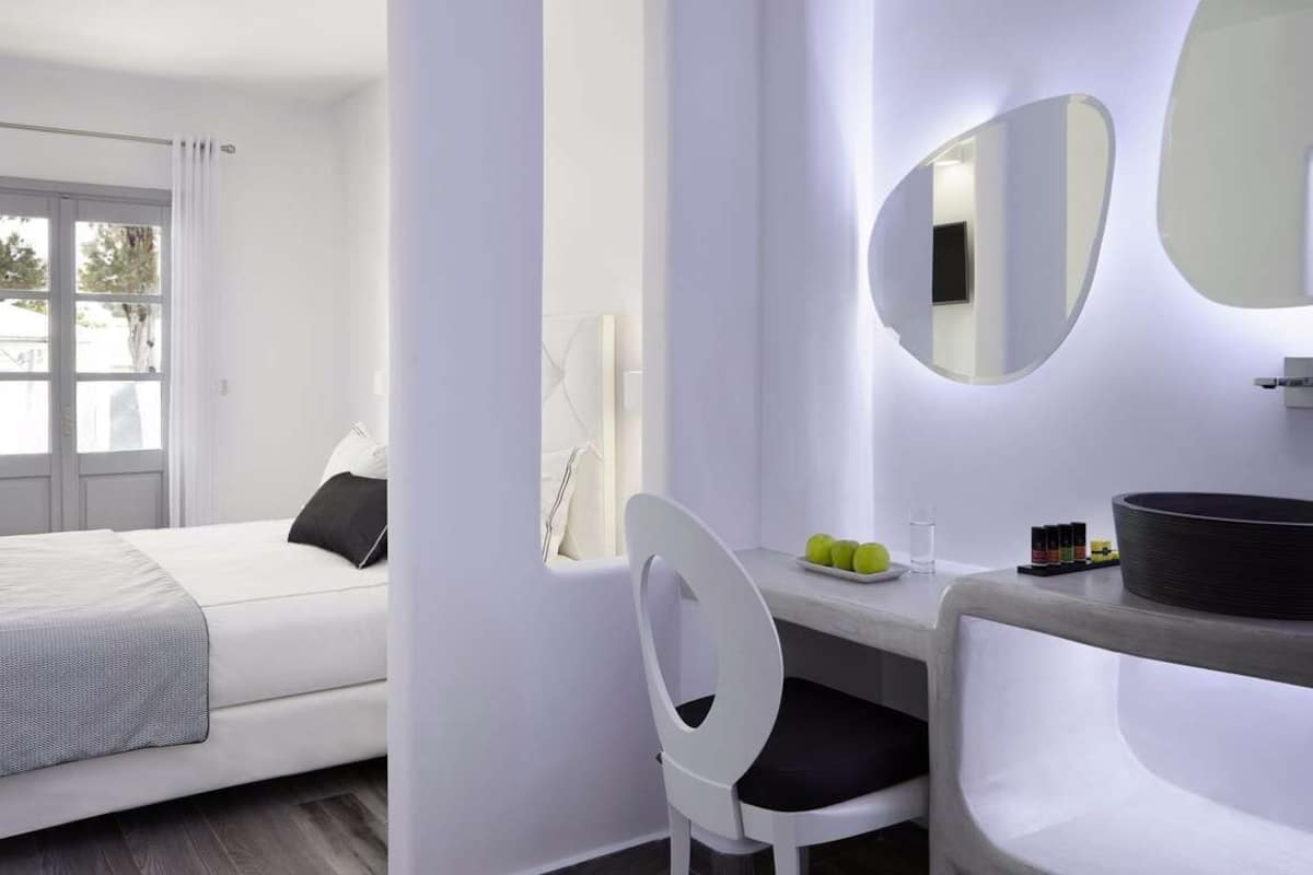 Una habitación de hotel moderna con una cama, un escritorio con silla, un espejo grande y una ventana con cortinas.