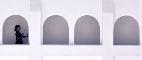A person carrying a tray with items in a modern, minimalist room with white walls and arched niches.