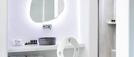 A bathroom with a white vanity, a round mirror, and a white chair.