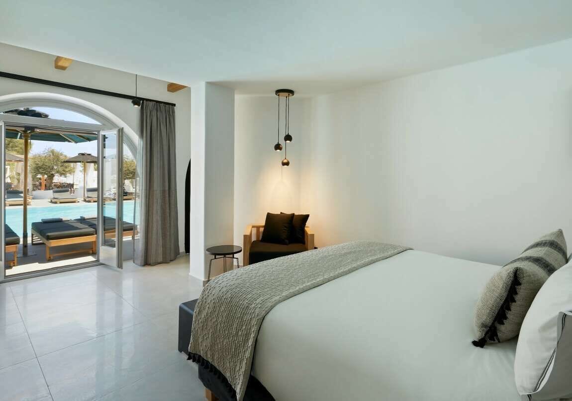 A modern hotel room with a large bed, a small desk, and a view of a pool area.
