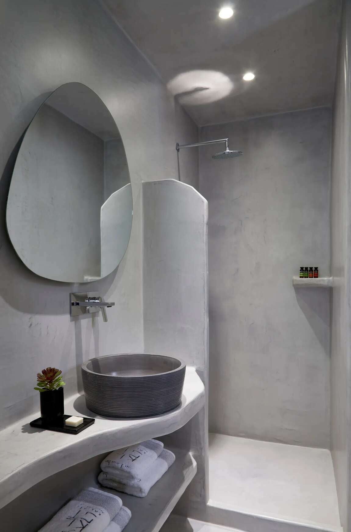 A modern bathroom with a round mirror, a vessel sink, and a shower area.