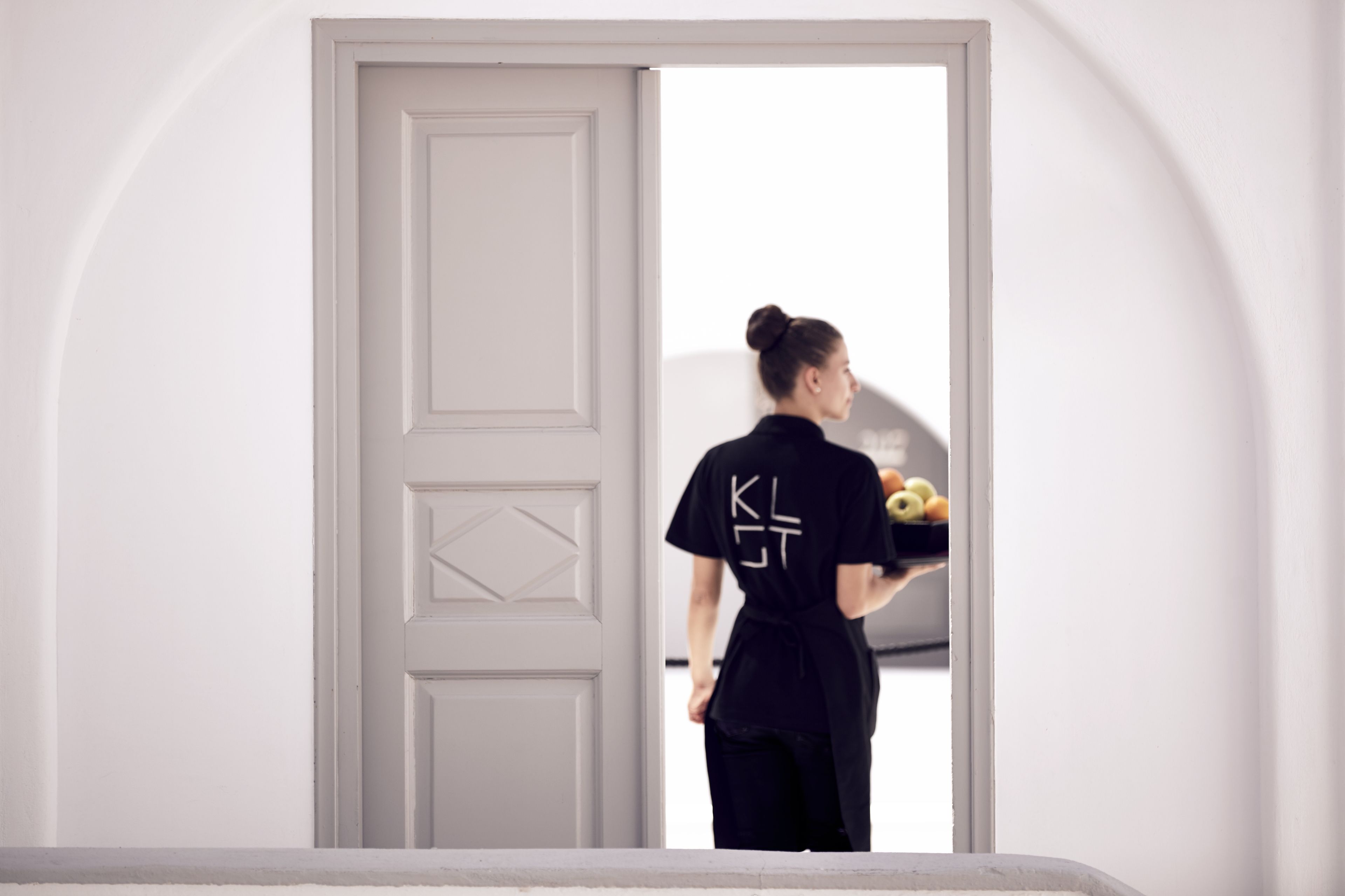 A person in a black shirt with a logo standing in a doorway.