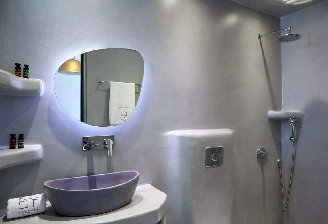 A modern bathroom with a round mirror, a vessel sink, and a shower.