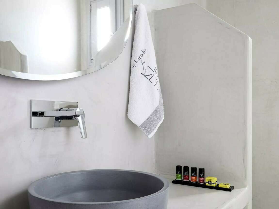 A modern bathroom with a round sink, a mirror, a towel, and a shelf with toiletries.