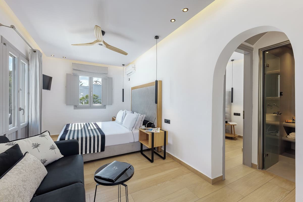 Un dormitorio moderno con cama, sofá, escritorio y un baño visible a través de un arco.