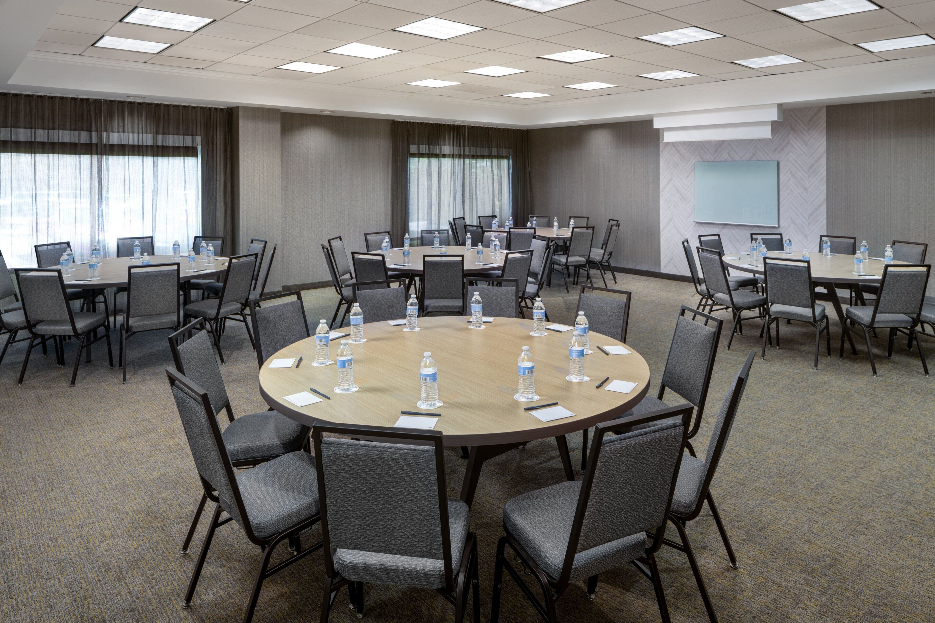 A conference room with multiple round tables, each equipped with chairs and water bottles.