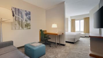 A hotel room with a sofa, a desk, a chair, a bed, a TV, and a painting on the wall.