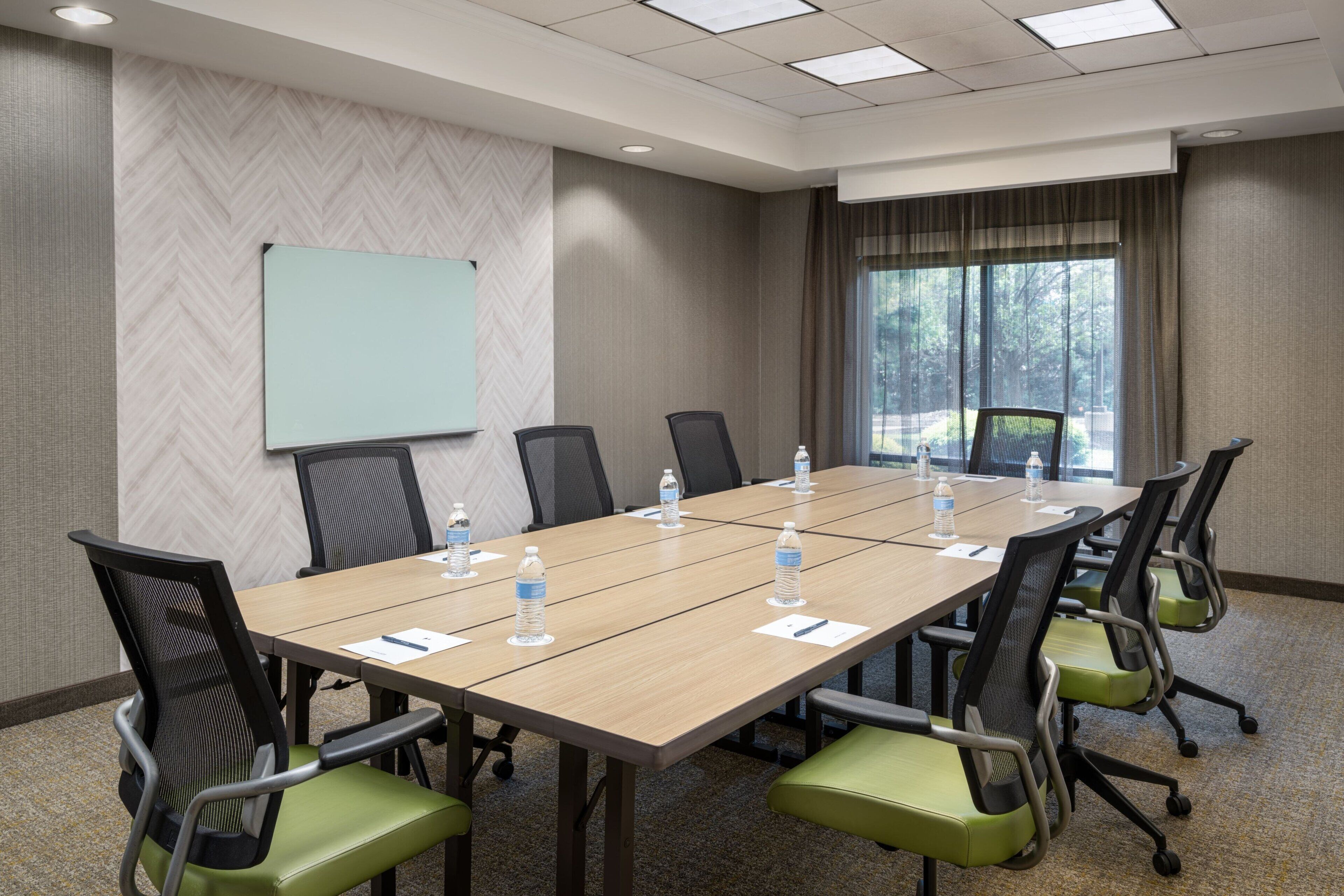 A conference room with a long table, chairs, a projector screen, and a window with curtains.