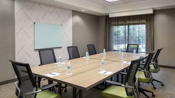 A conference room with a long table, chairs, a projector screen, and a window with curtains.