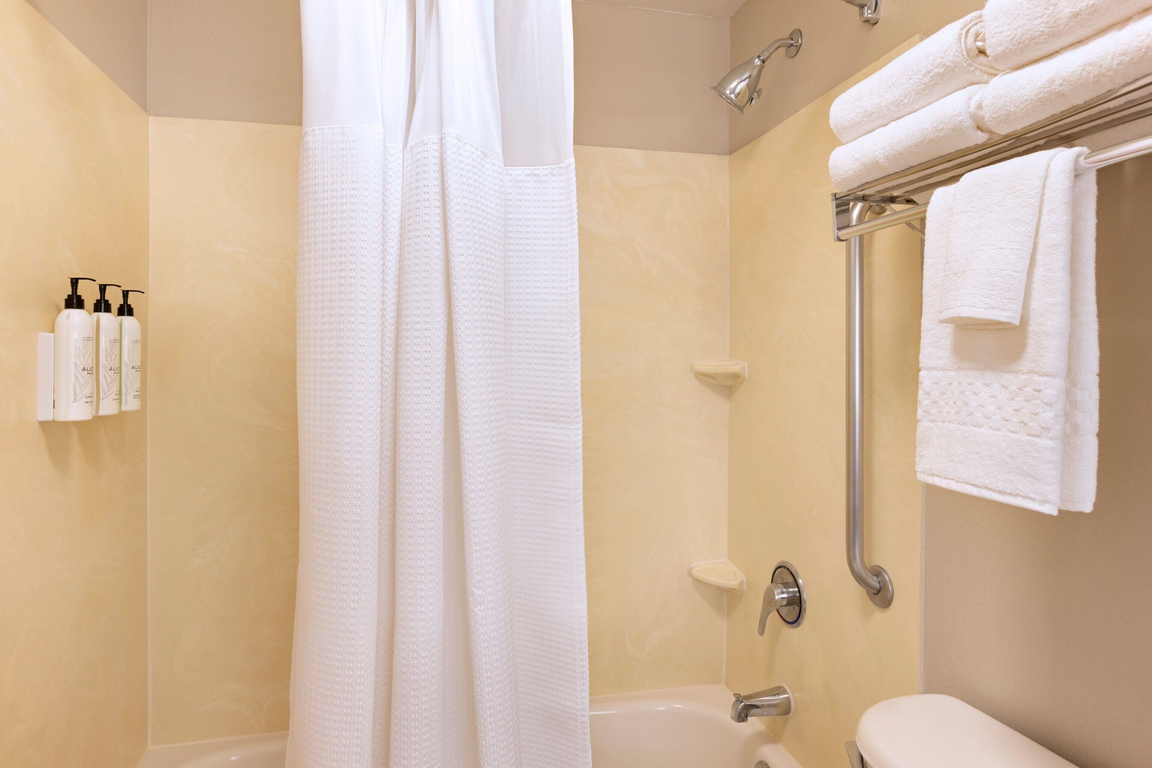 A bathroom with a shower, a bathtub, and a toilet. There are towels on a rack and toiletries on the wall.