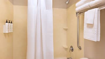 Un baño con ducha, bañera y retrete. Hay toallas en un perchero y artículos de aseo en la pared.
