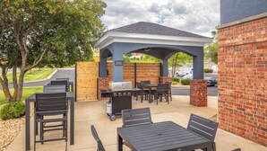 An outdoor patio with a covered seating area, a grill, and a table with chairs. - Candlewood Suites St Robert by IHG (St. Robert)