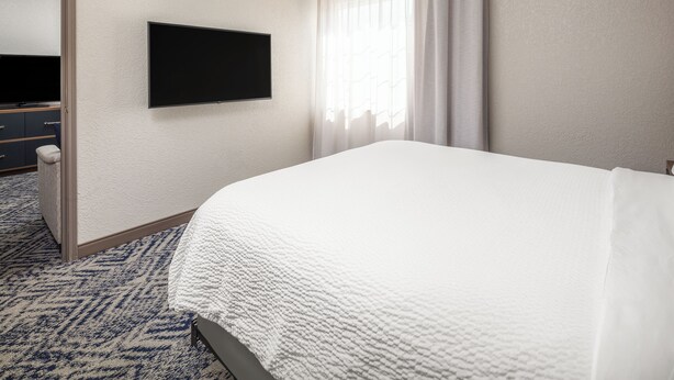 A hotel room with a bed, a flat-screen TV mounted on the wall, a door, and a window with curtains. - Candlewood Suites St Robert by IHG (St. Robert)
