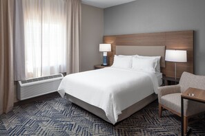 Ett hotellrum med en stor säng, två sänglampor, en stol och ett fönster med gardiner.
