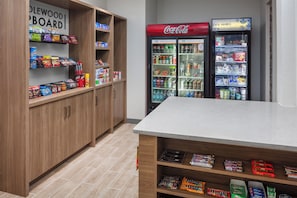 A snack bar area with shelves stocked with various snacks and a Coca-Cola refrigerator. - Candlewood Suites St Robert by IHG (St. Robert)