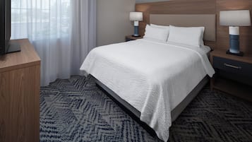 A hotel room with a bed, nightstands, lamps, a TV on a stand, and a window with curtains.
