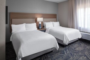 A hotel room with two beds, a nightstand with a lamp, a wall-mounted heater, and a window with curtains. - Candlewood Suites St Robert by IHG (St. Robert)