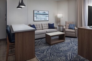 A modern hotel room with a sofa, armchair, coffee table, and a large window. - Candlewood Suites St Robert by IHG (St. Robert)
